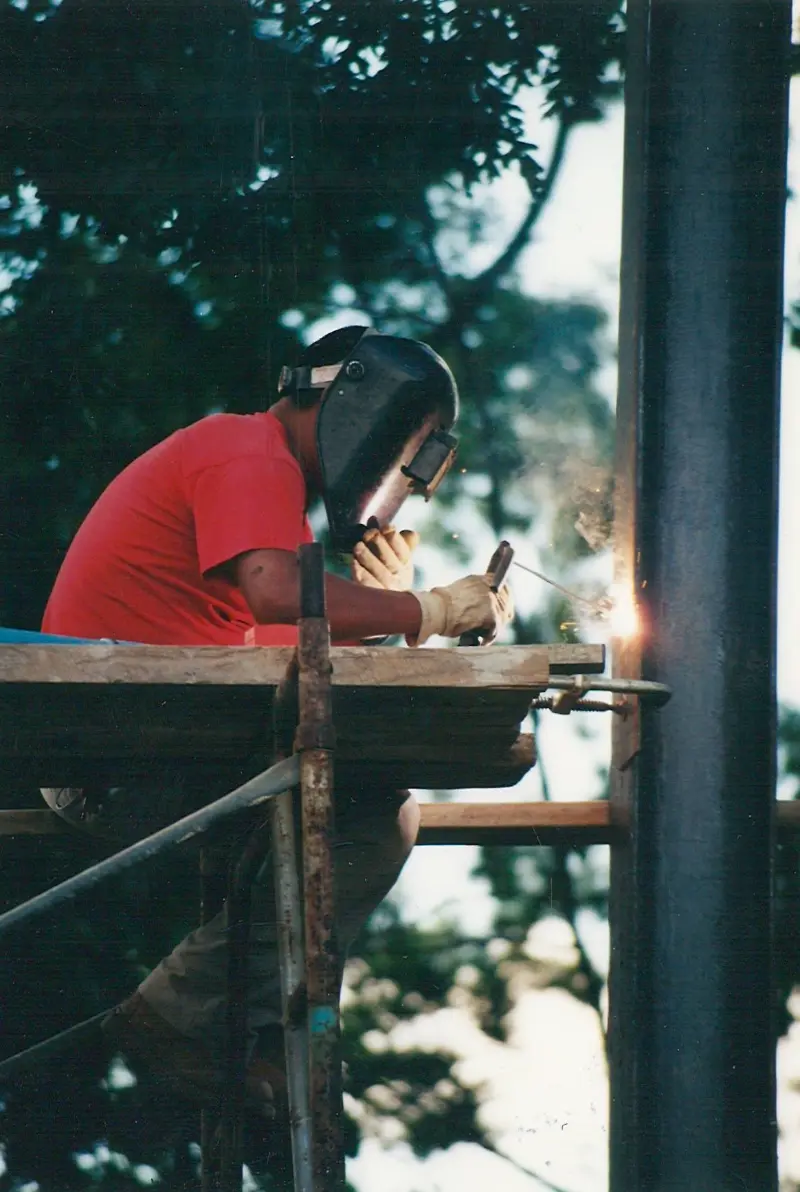 Worker welding on scaffold, sparks falling.