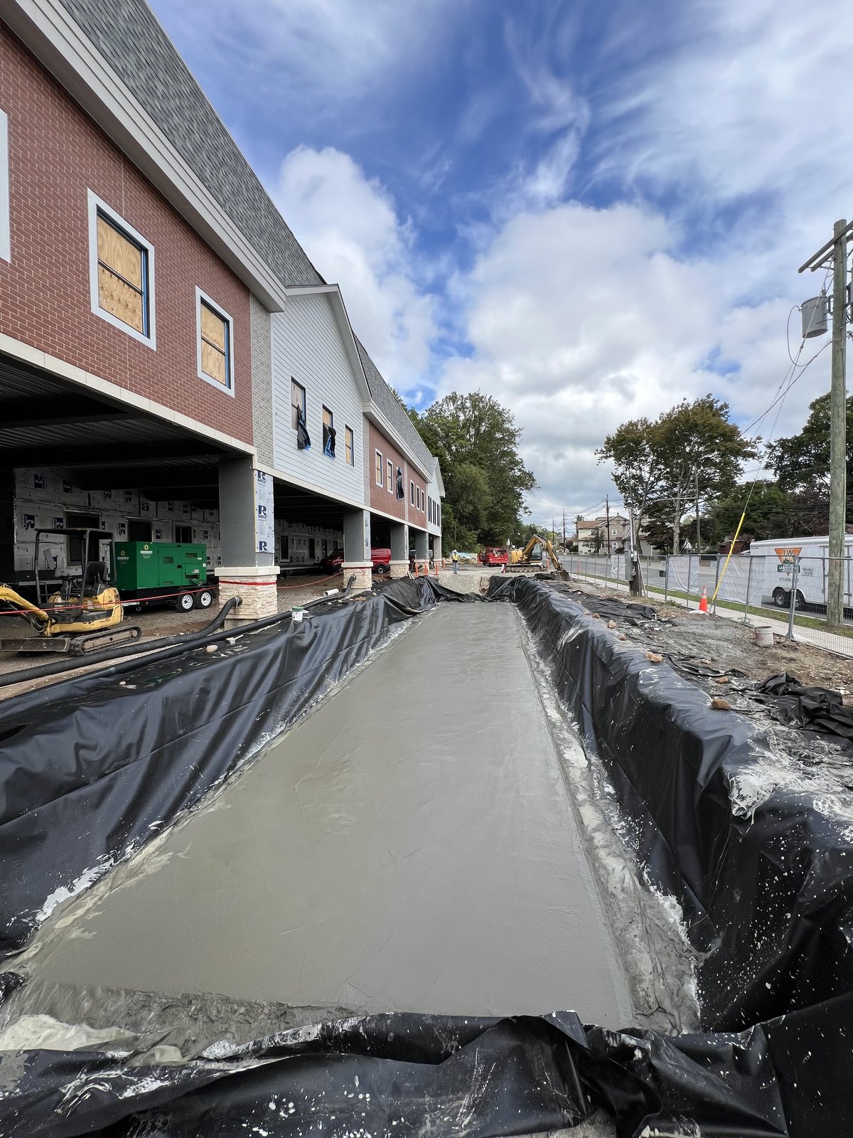 Sidewalk concrete pour along the red-brick and white-siding facade of Trojan Storage.